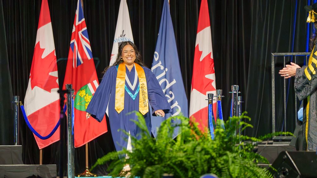Valedictorian Tilly Millena walks across the stage in front of several flags.