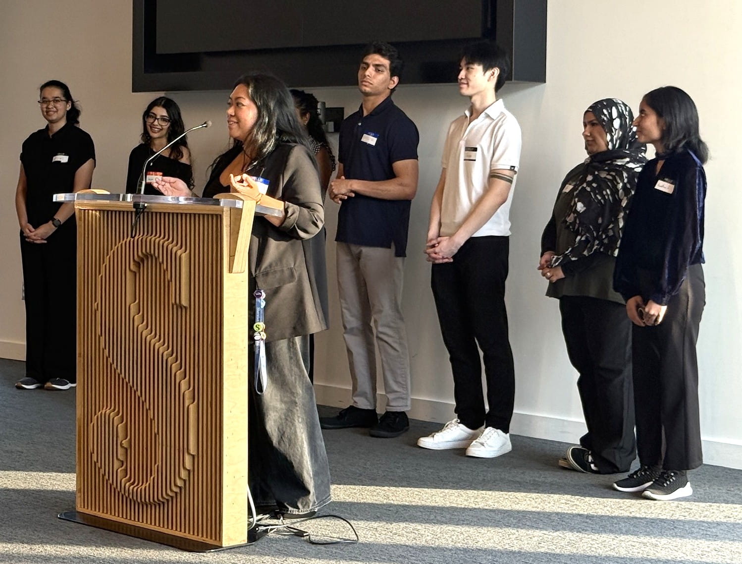 Valedictorian Tilly Millena stands at a podium giving a presentation with several group members standing behind her.