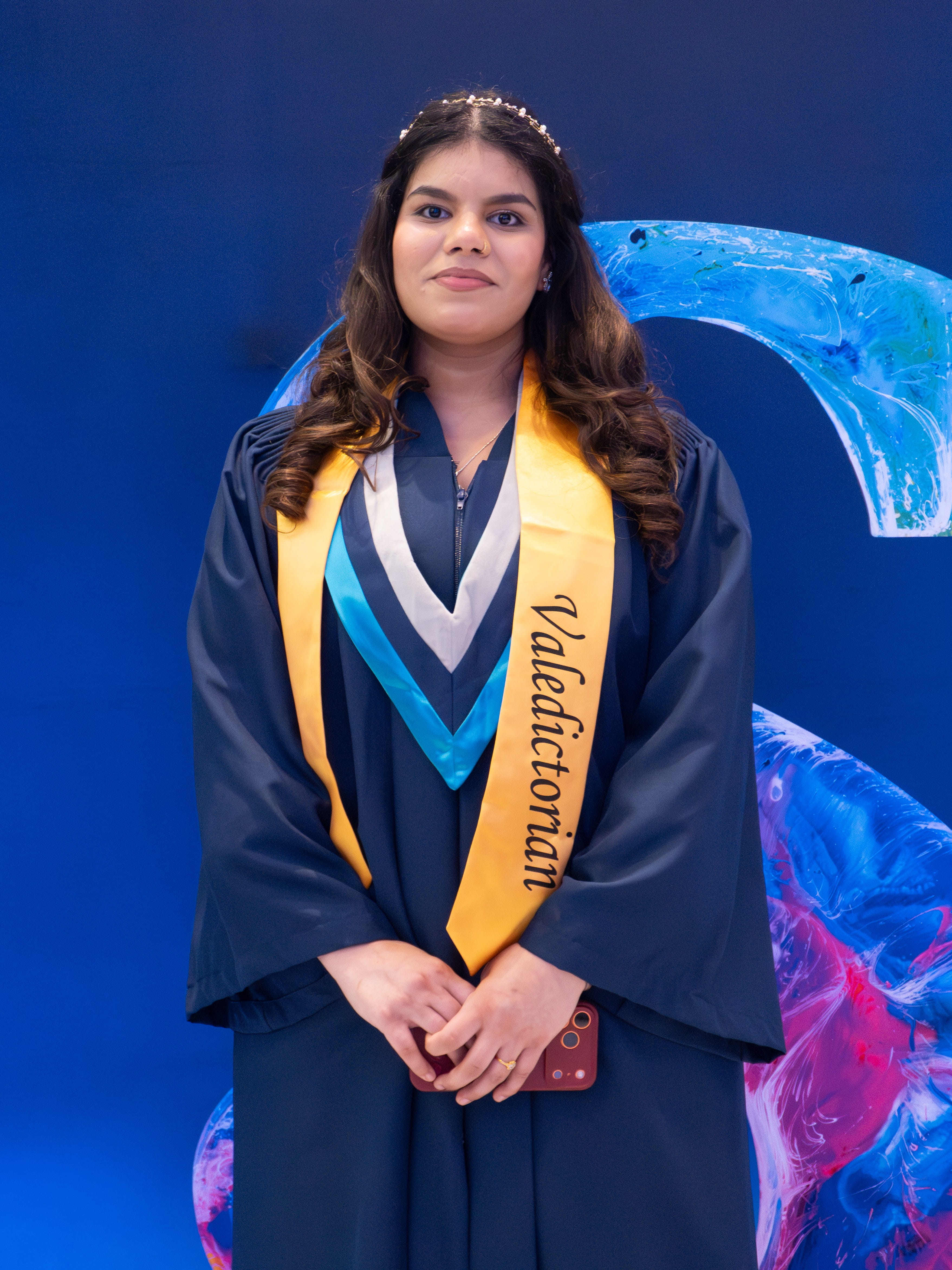 Valedictorian Lovepreet Dhillon stands in front of a branded Sheridan S sign.