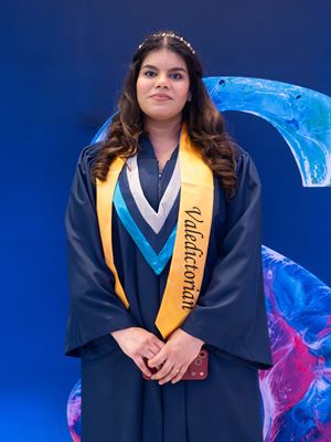 Valedictorian Lovepreet Dhillon stands in front of a branded Sheridan S sign.