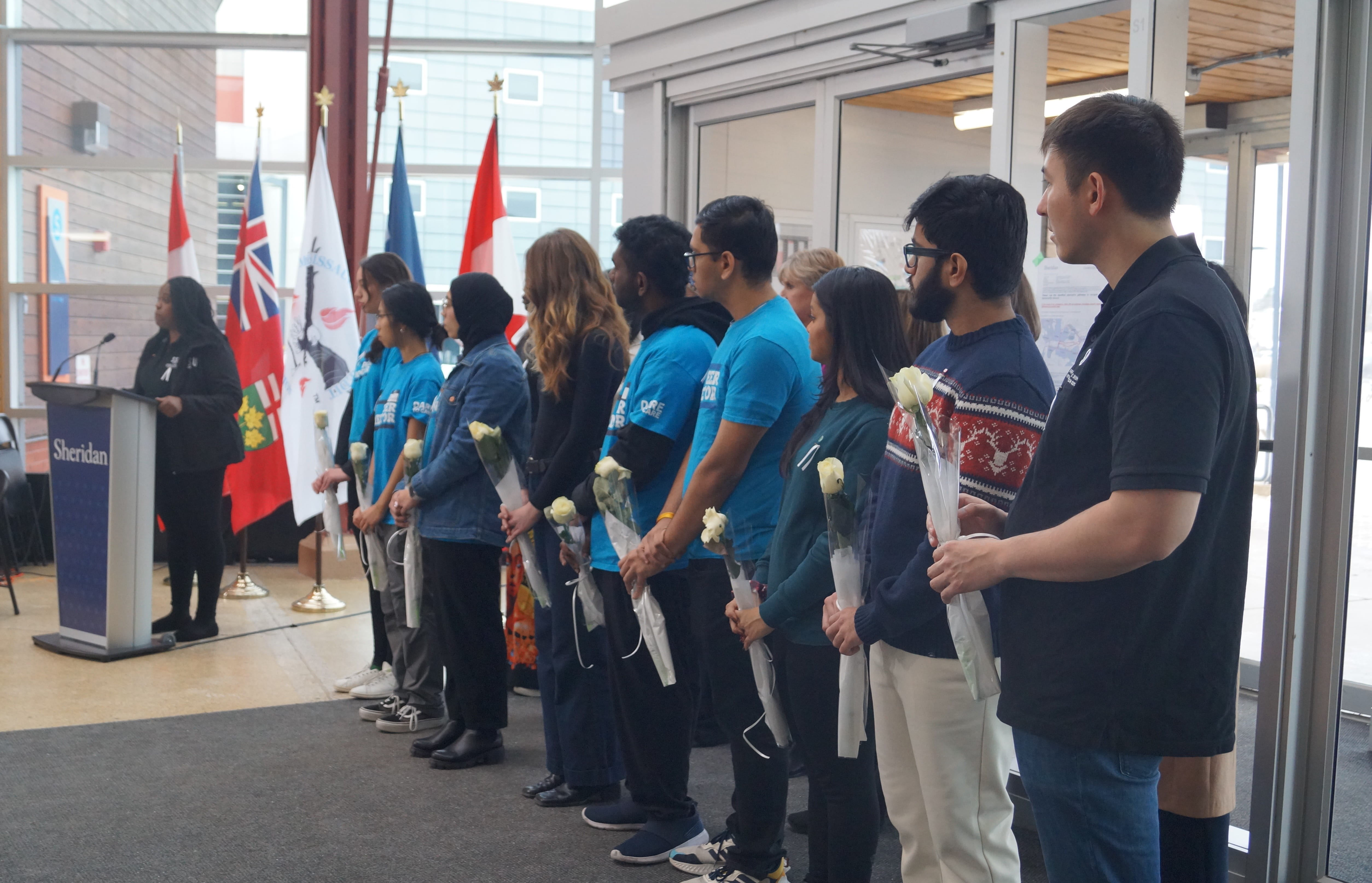 Amalia Powell stands at the podium in the background and people holding roses stand in the foreground.
