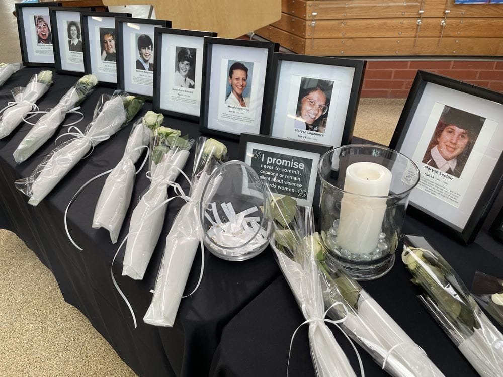 A row of framed photos of the victims is lined up on a table, with a white rose in front of each one, along with a white candle.