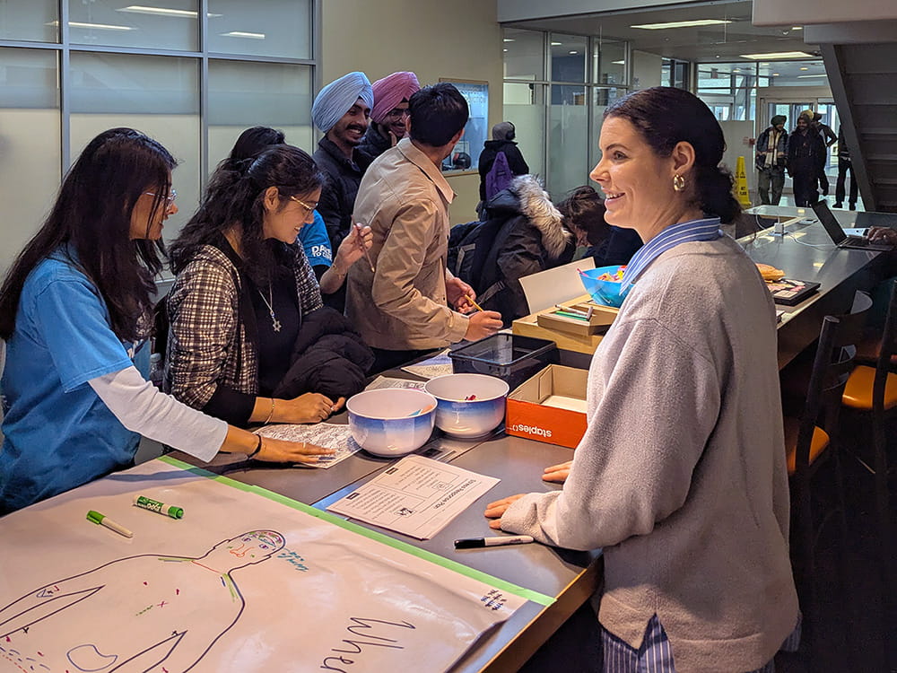 Erin Lind stands across the table from a group of students working on an activity