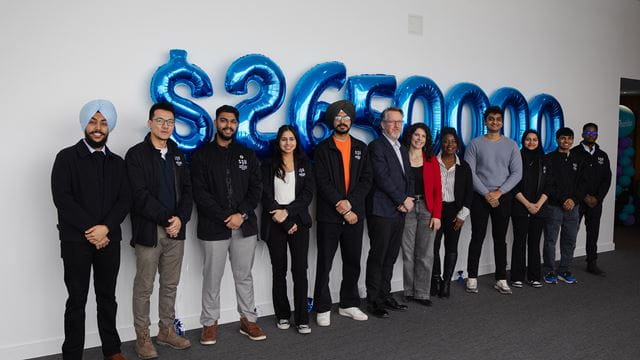 Group standing side-by-side against a wall with balloons in the shape of numbers behind them