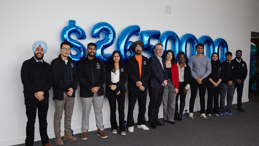 Group standing side-by-side against a wall with balloons in the shape of numbers behind them