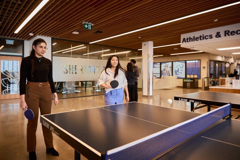 Two female students play ping pong in the athletics facility at Hazel McCallion Campus