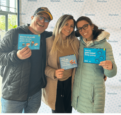Three Sheridan students hold up the the Kind Mail postcards they received