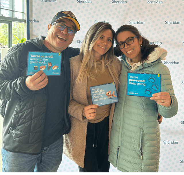 Three Sheridan students hold up the the Kind Mail postcards they received