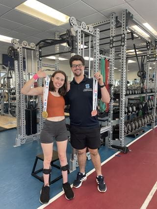 Marino Bortolussi and an athlete stand inside the Sheridan fitness centre holding medals