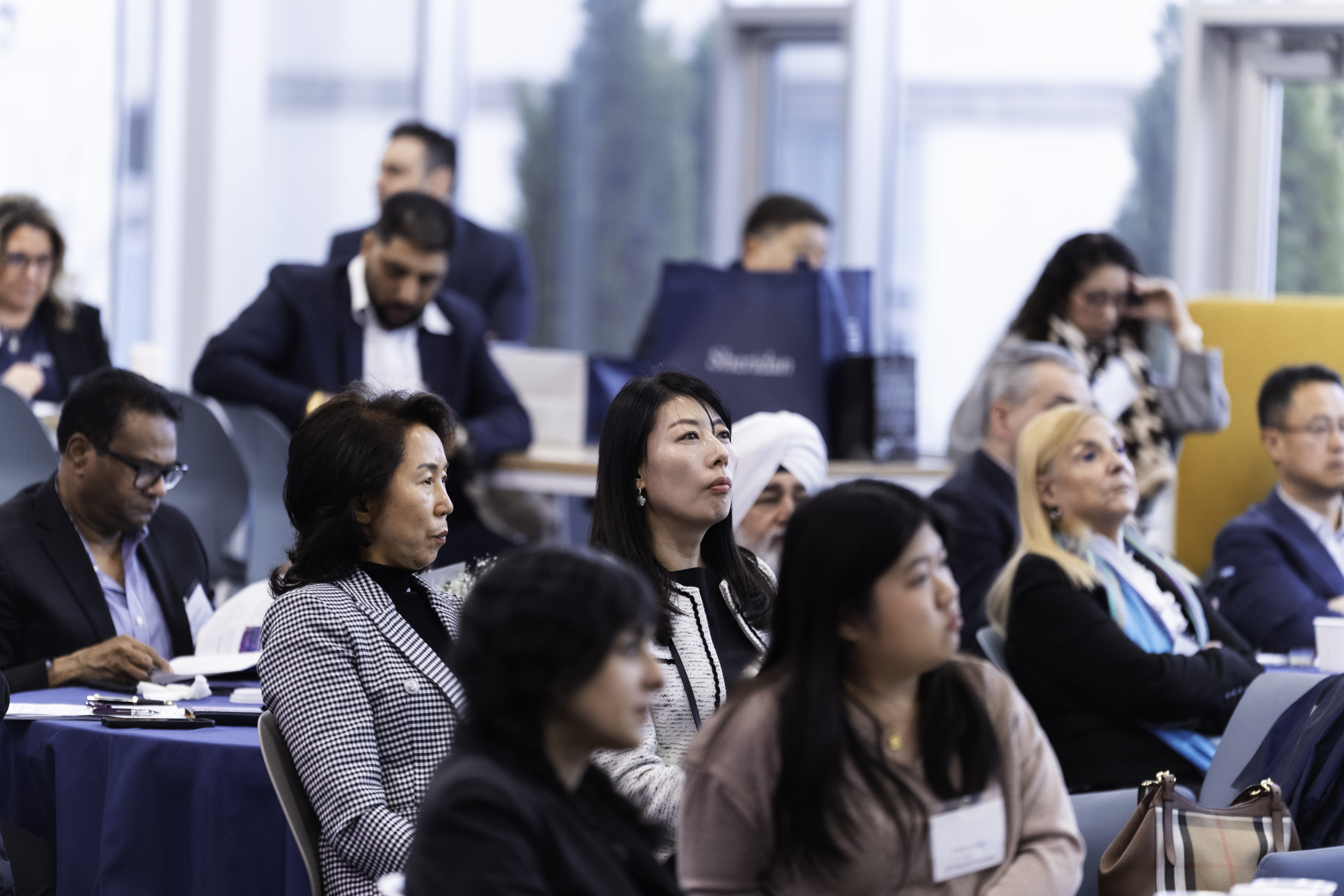 People sitting at tables look towards a speaker at the front of the room.