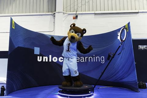 Bear mascot Bruno stands in front of a blue banner that says unlock learning.
