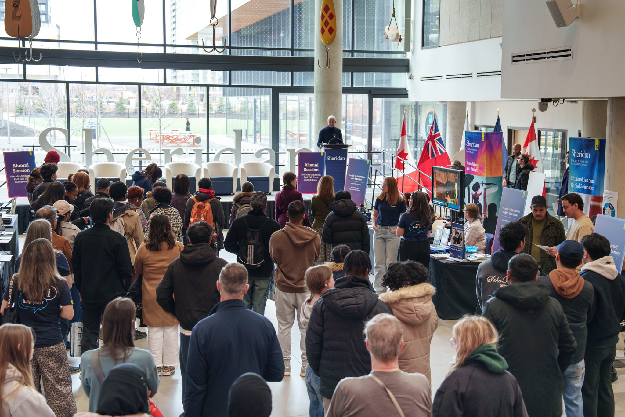 A crowd of people face a speaker on stage at HMC campus.