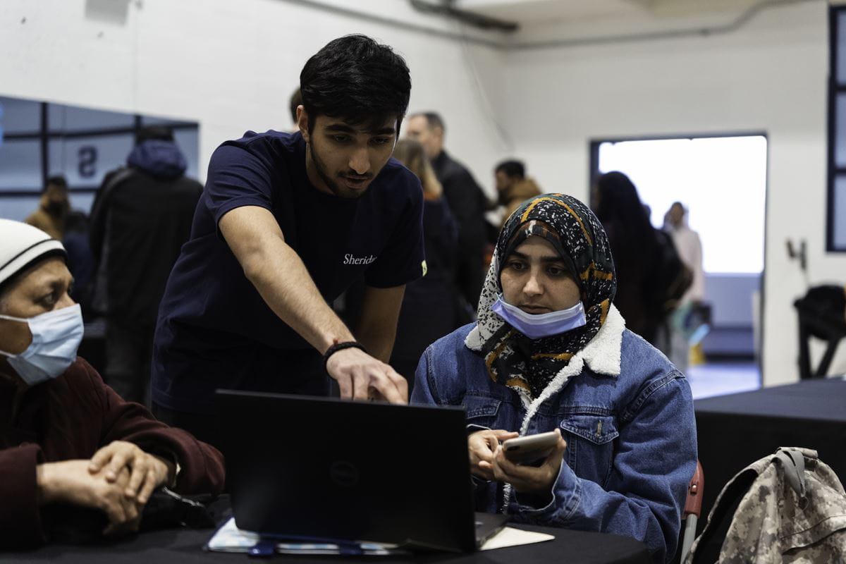 A male student points at a laptop screen that a female student is working on.