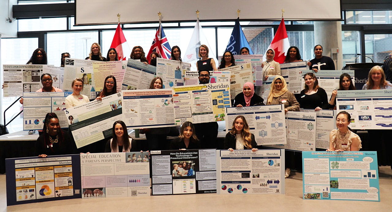 Early Childhood Leadership students gather together on a stage for a group photo with their capstone project posters.