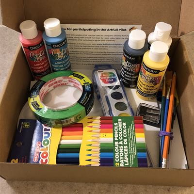 Box of art supplies including paints, coloured pencils and tape