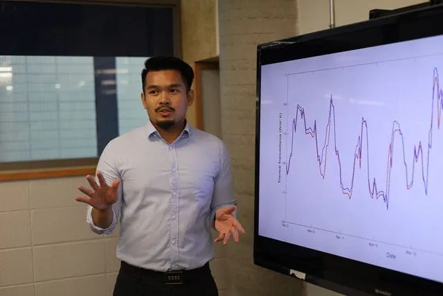 Mechanical Engineering student Daniel Ta stands next to a screen displaying his research findings