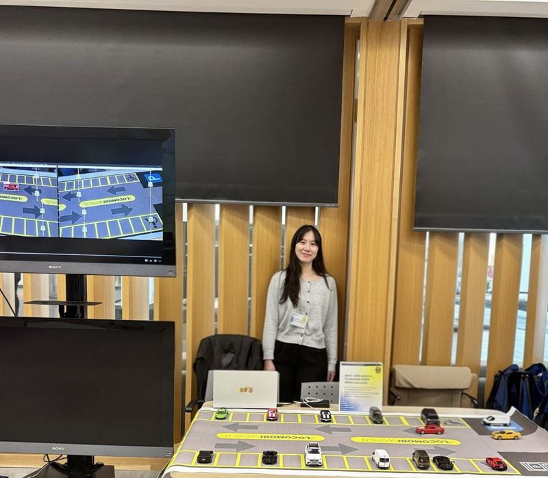 Sheridan student Dohee Kim stands behind a table displaying the vehicle tracking solution she helped build to improve parking systems