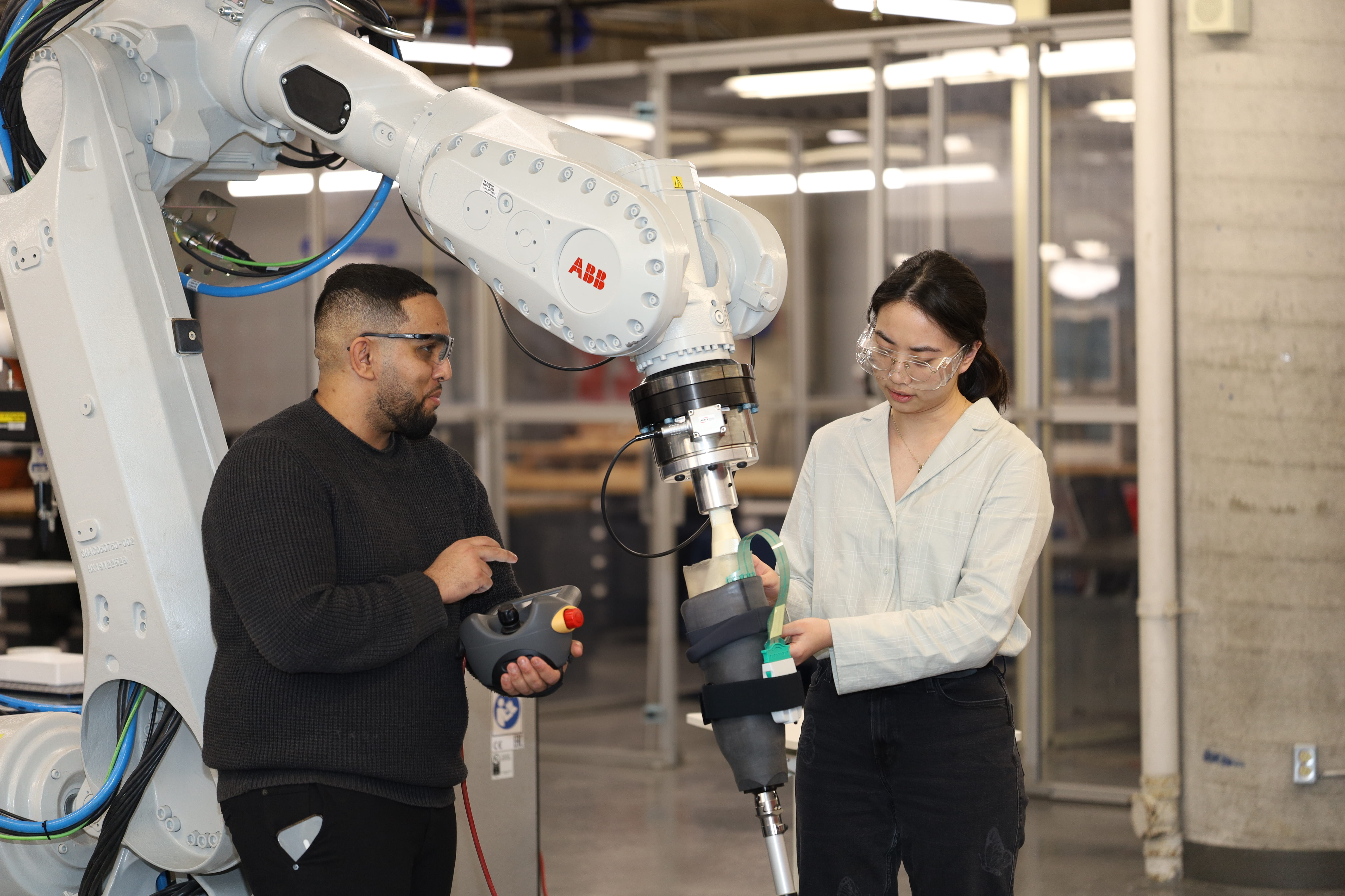 Two researchers examine how a prosthetic limb moves during a gait simulation powered by a robotic arm