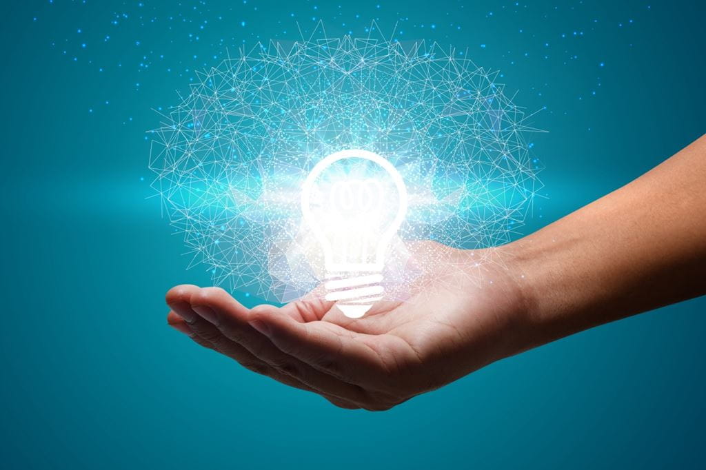 A person's hand holds a shining light bulb, representing innovation