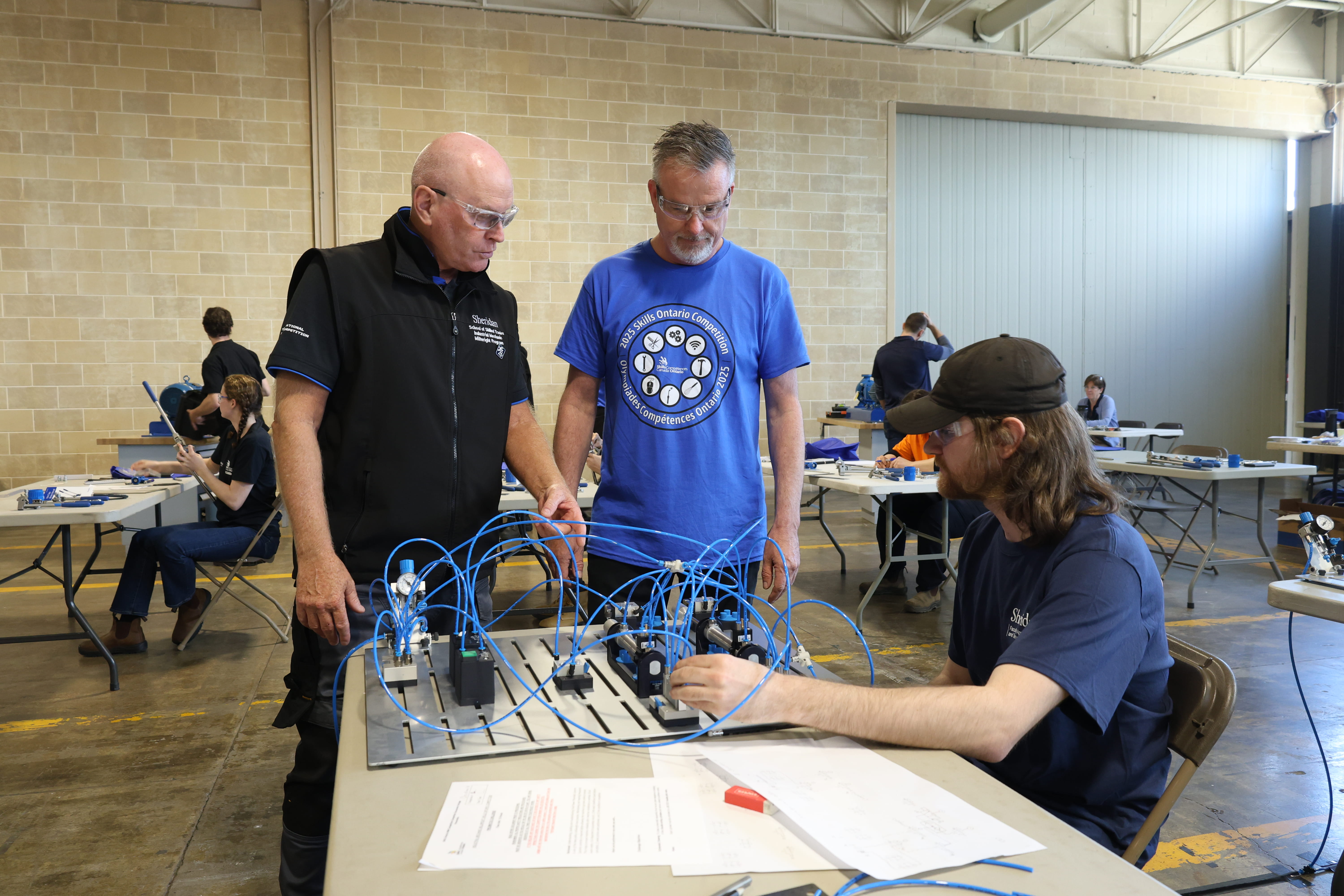 Sheridan Interim Associate Dean Craig Brazil and another person judge the work of a student in the Industrial Mechanics Millwright event.