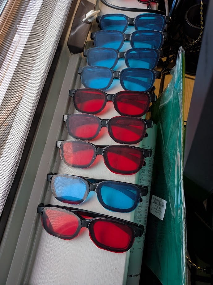 Pairs of anaglyph rendering glasses are lined up side by side, some with two blue lenses and some with two red lenses