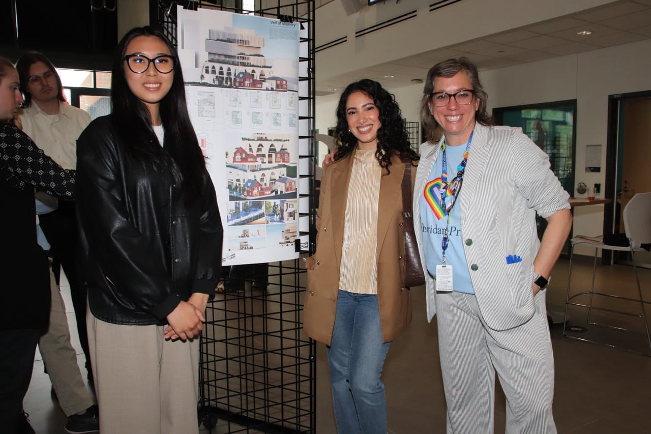 students and professors stand next to a display of a project