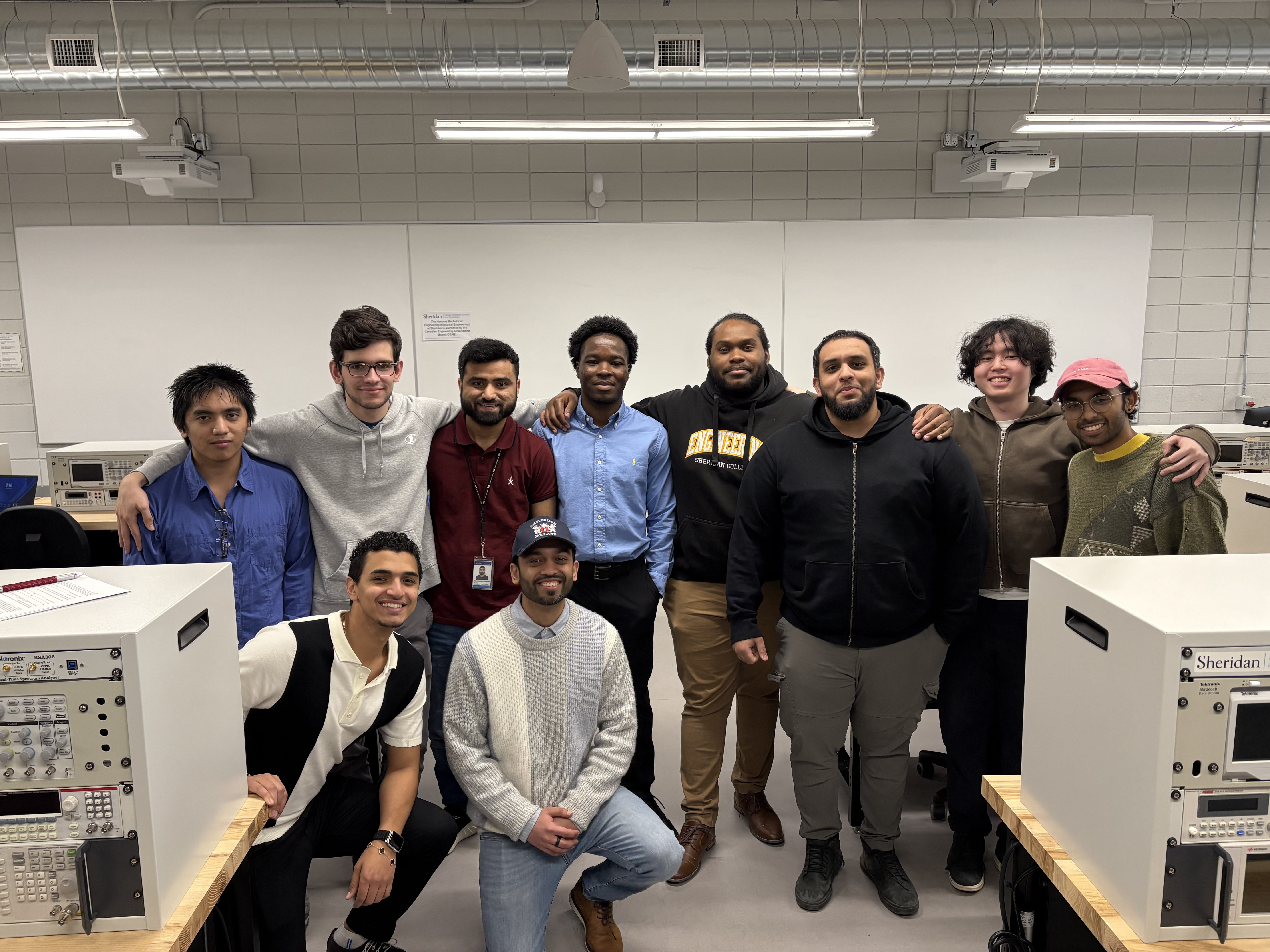 Ten engineering students stand together as a group in an engineering lab.