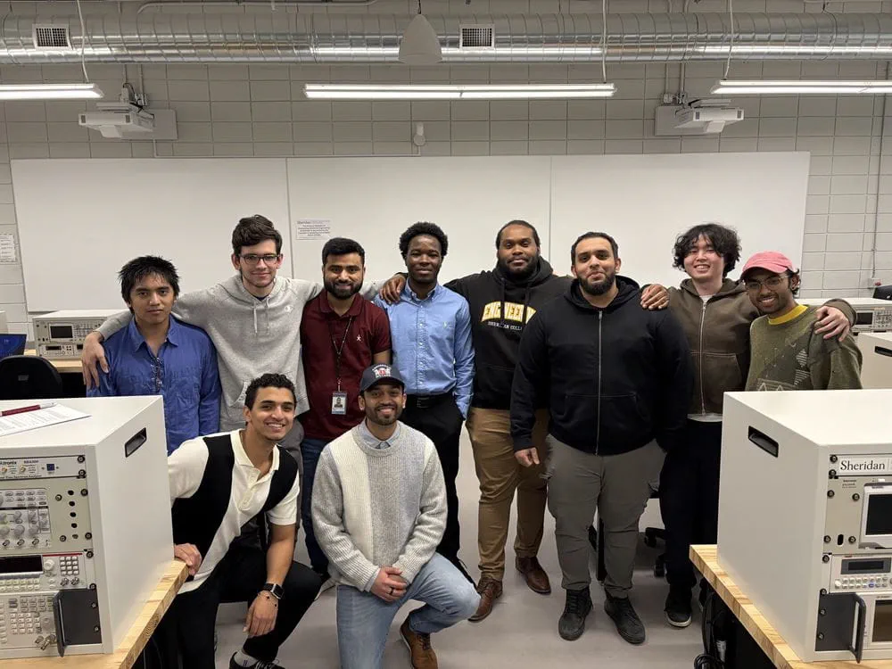 Ten engineering students stand together as a group in an engineering lab.