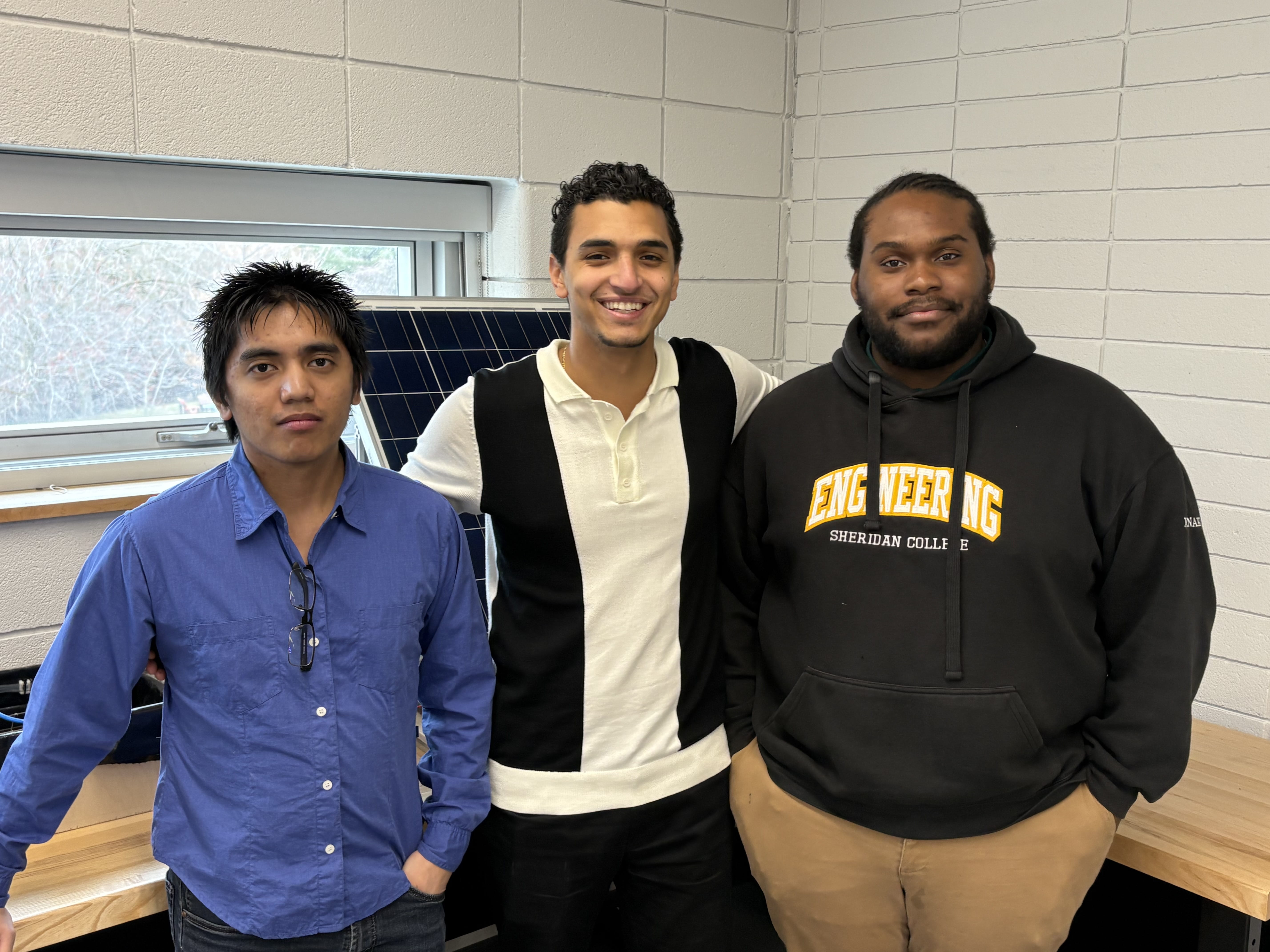 Three engineering students stand in front of their solar panel project.