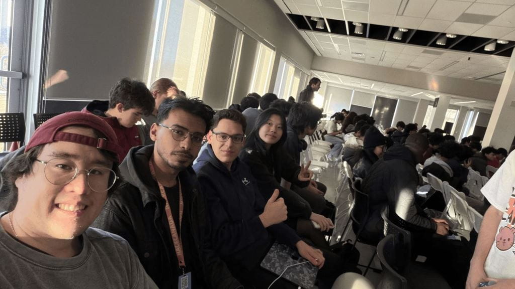 The four members of the Ember team smile for the camera while seated in a large room during a hackathon