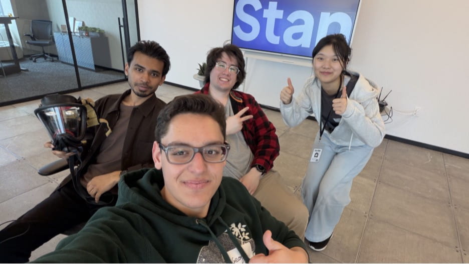 The four members of the Ember team pose for a photo in front of a Stan sign