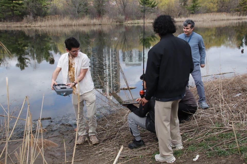 Three students prepare to launch their boat into the pond on Sheridan's Davis Campus.