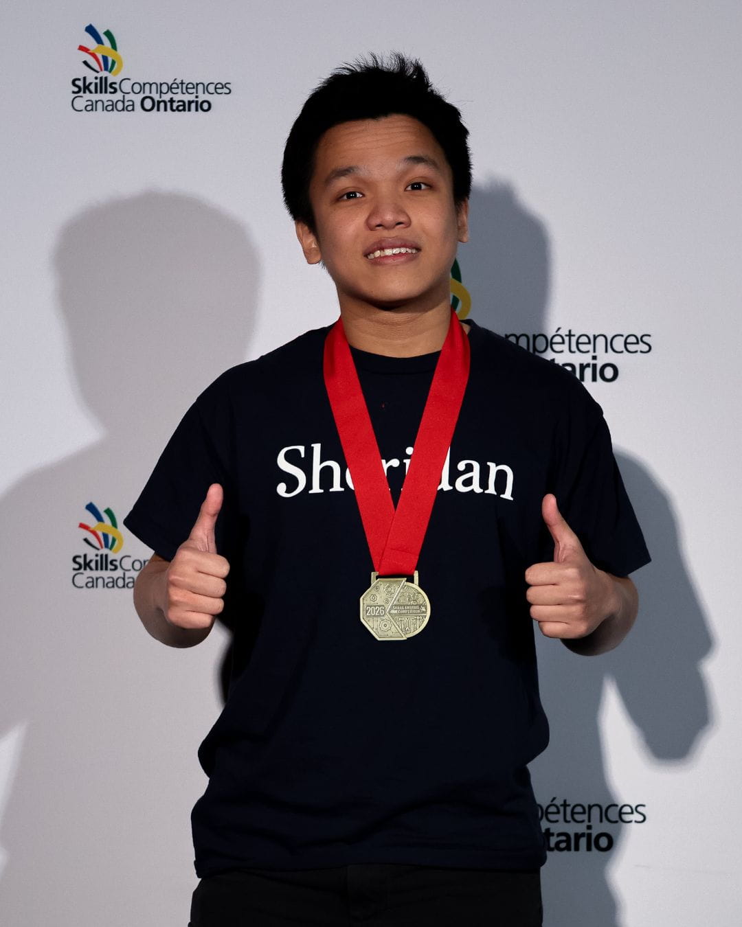 Sheridan student Thinh Luu smiles and gives two thumbs up while wearing his gold medal