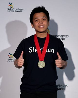 Sheridan student Thinh Luu smiles and gives two thumbs up while wearing his gold medal