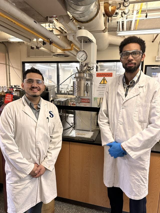 Chemical engineering technology student researchers Vikram Pandey and Hughroy Staple stand in front of a batch reactor in one of Sheridan's chemical engineering labs