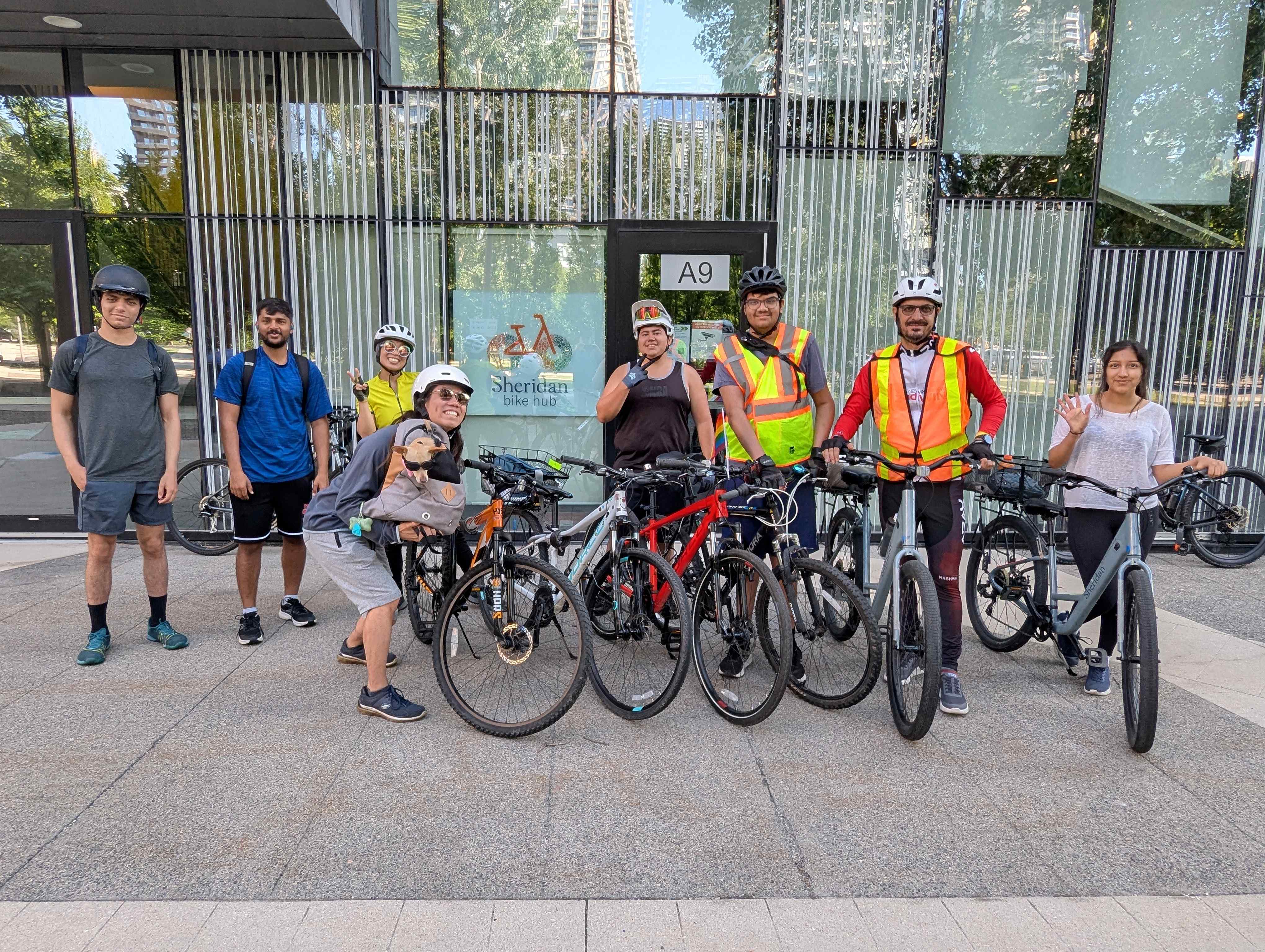 A group of people with bikes stand in front of a campus building.