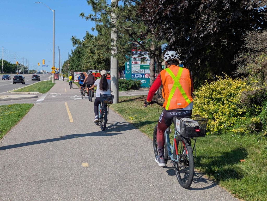 Several cyclists ride down a multi-use path beside a road.