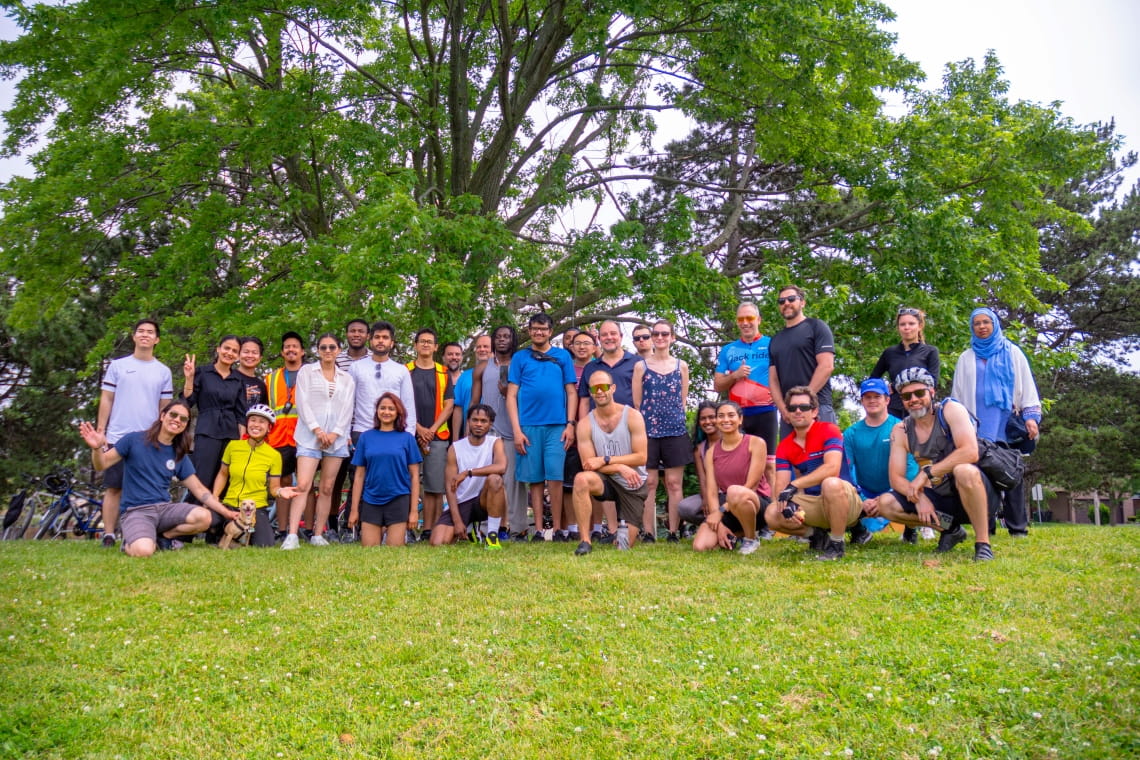 A large group of cyclists pose for a photo in the park under a tree