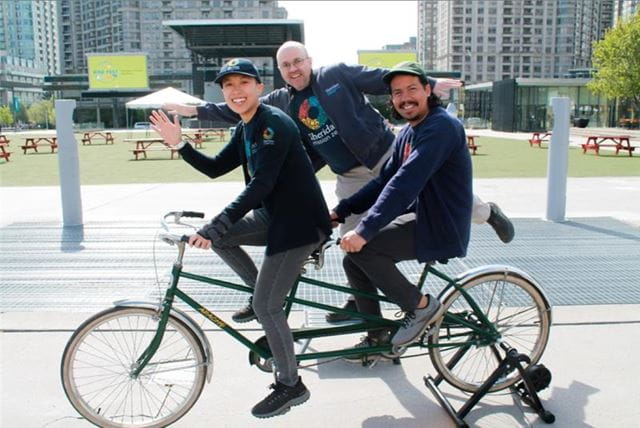 Three people from Sheridan Mission Zero pose with a tandem bike on campus