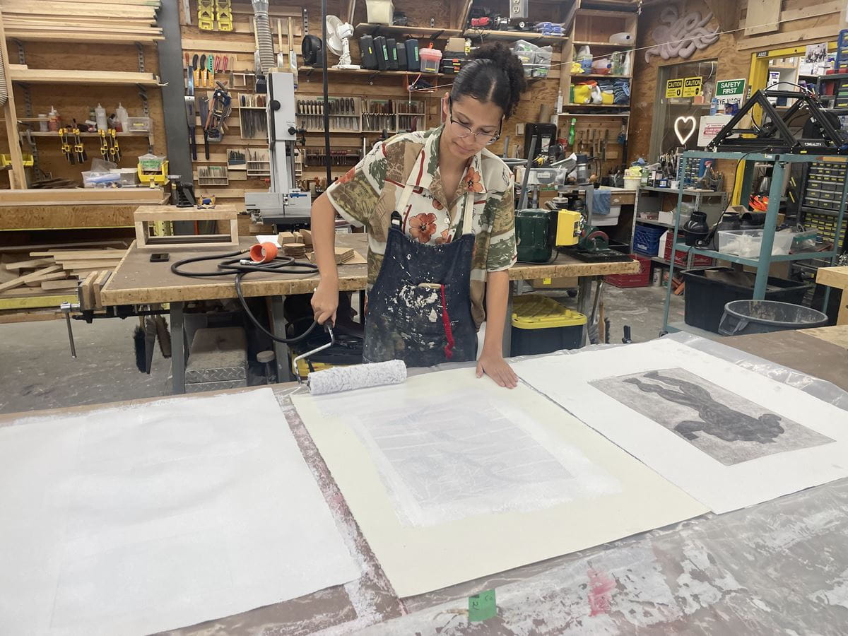 A student wearing an apron uses a roller paint brush to prime a canvas for reuse.