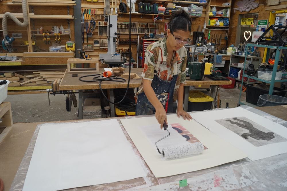 Student Martha Burchert uses a paint roller brush to prime a previously used canvas, turning it white to be used again.