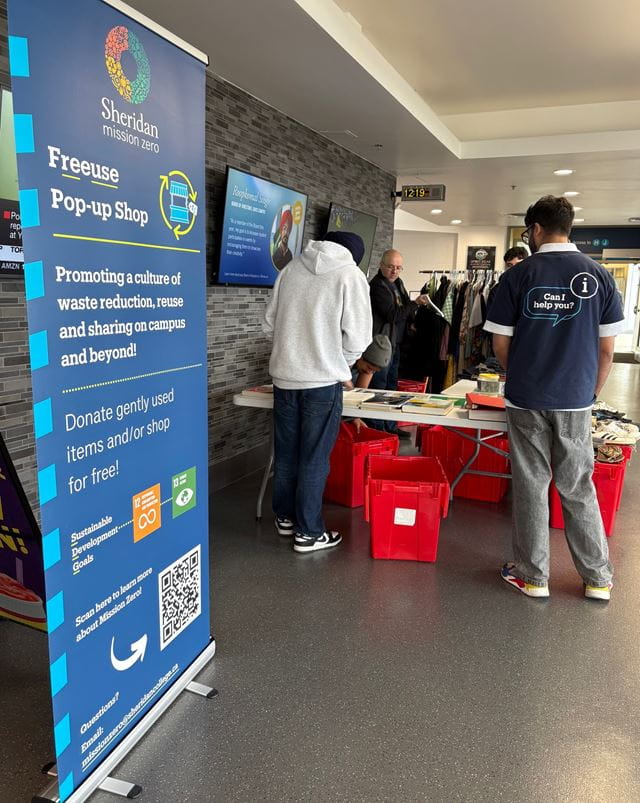 A poster which says Freeuse Pop-Up Shop in front of a table with free items as people gather to look.