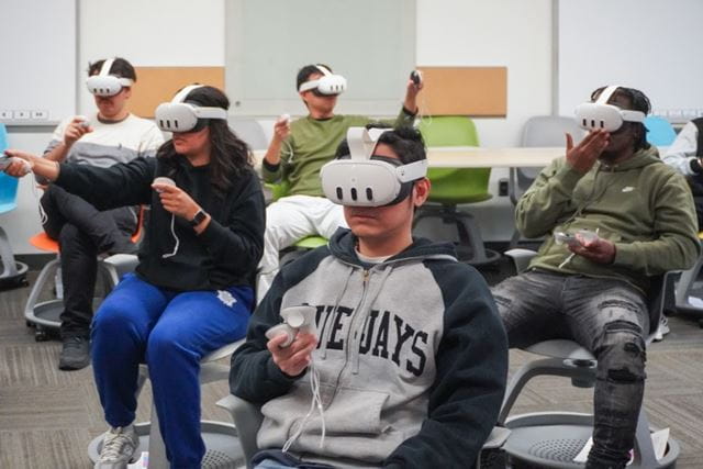 Students sit in chairs of a classroom while wearing Meta Quest 3 headsets to participate in virtual reality simulations