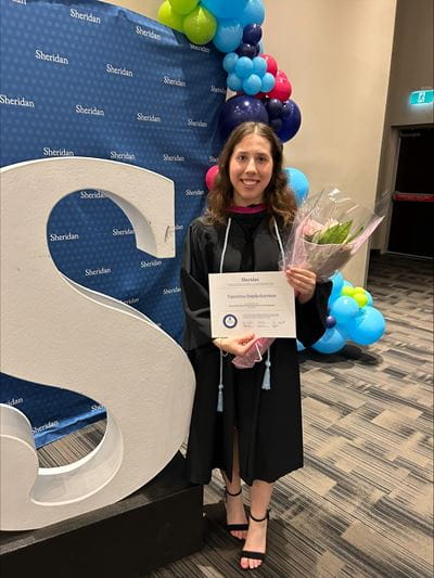 Valentina Depikolozvane stands beside the Sheridan 'S' at Convocation while holding her degree