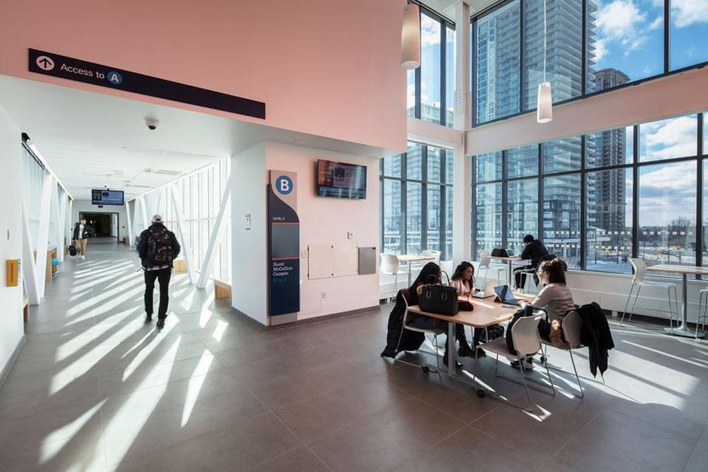 Four students sit at a study table at HMC Campus, while another student walks down a hallway.