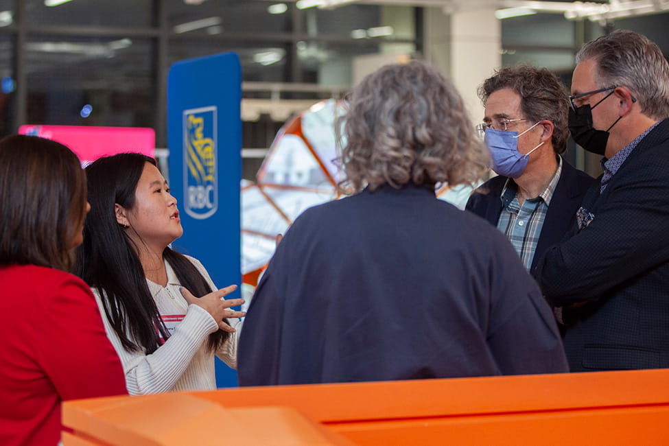 A group of 5 people having a conversation. An RBC sign can be seen in the background.