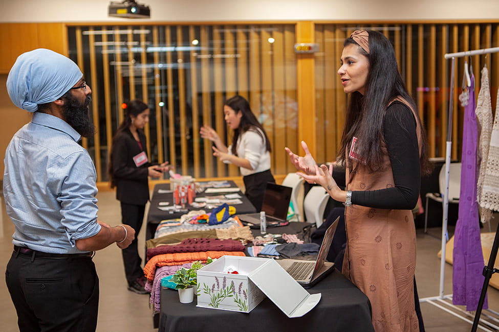 Two people talking with a table containing textiles between them