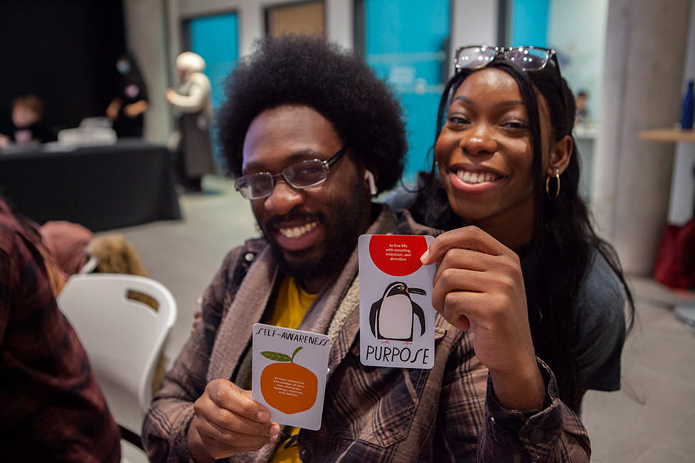 Two people holding up cards that say 'SELF-AWARENESS' and 'PURPOSE'