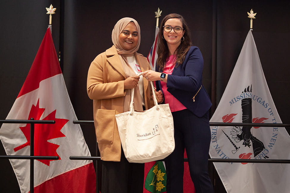 MPP for Mississauga Centre Natalia Kusendova posing with another person. They are holding a Sheridan EDGE bag in front of them.