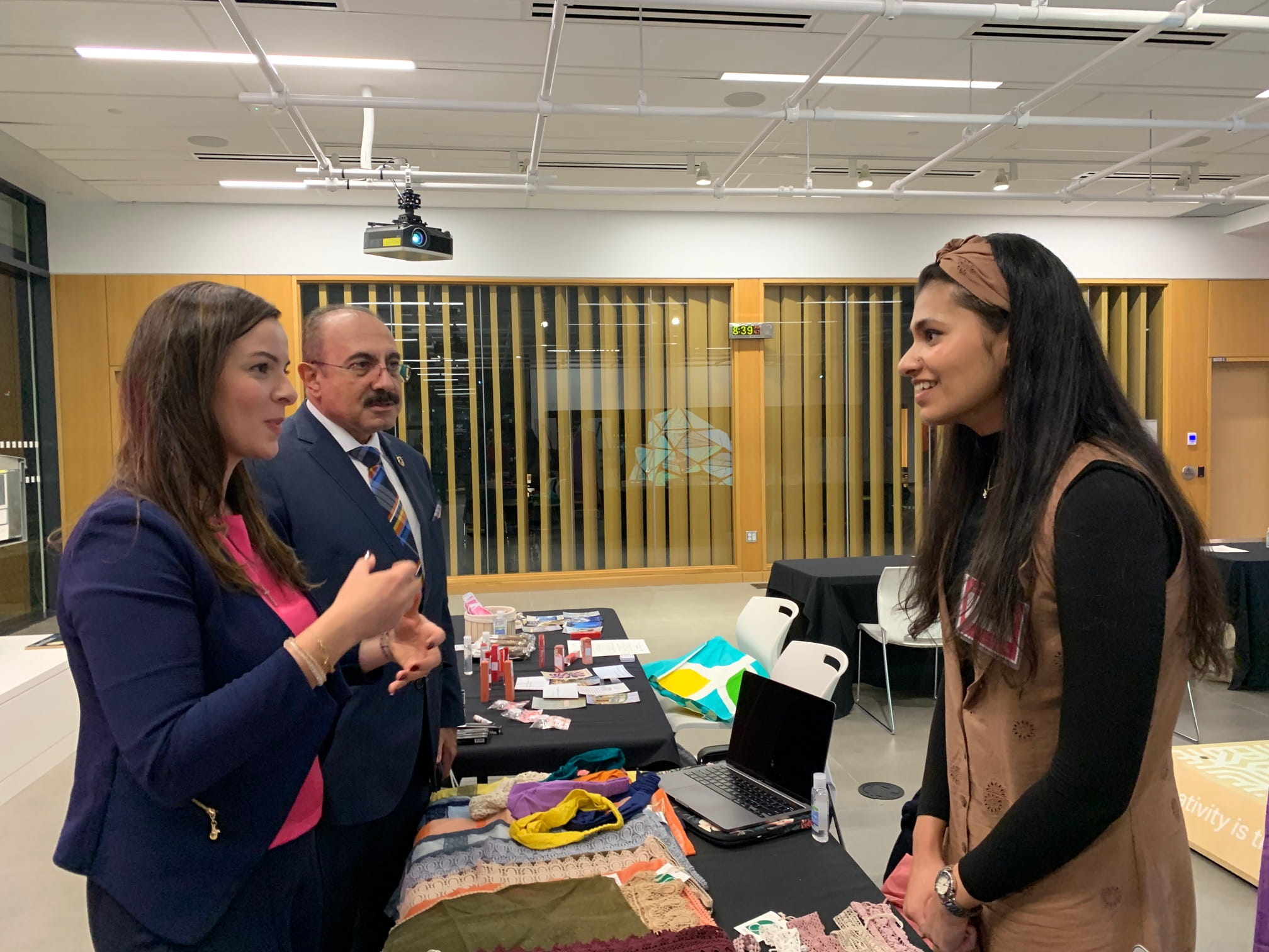 Three people talking with a table containing textiles between them